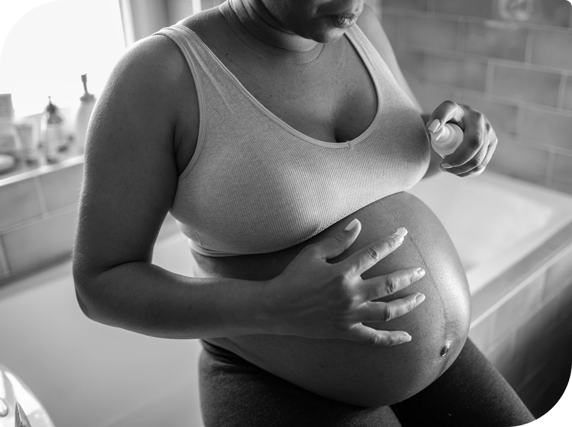 Pregnant woman applying lotion to belly.